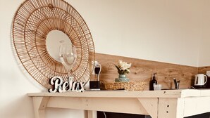 A wooden table with a woven mirror and a glass on it, a small plant, and a sign that says "Relax". - Country Studio Out West (Helensville)