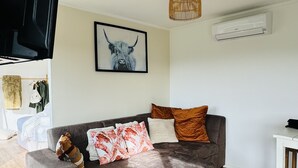 A modern living room with a grey sectional sofa, a mounted flat-screen TV, a wall-mounted air conditioner, and a framed artwork of a bull. - Country Studio Out West (Helensville)