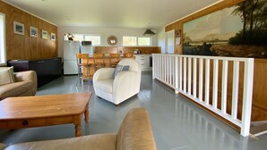 A spacious living area with a kitchen in the background, a white sofa, a wooden coffee table, and a white railing.