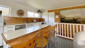 A modern kitchen with a large island, bar stools, and a view of the countryside through a large window.