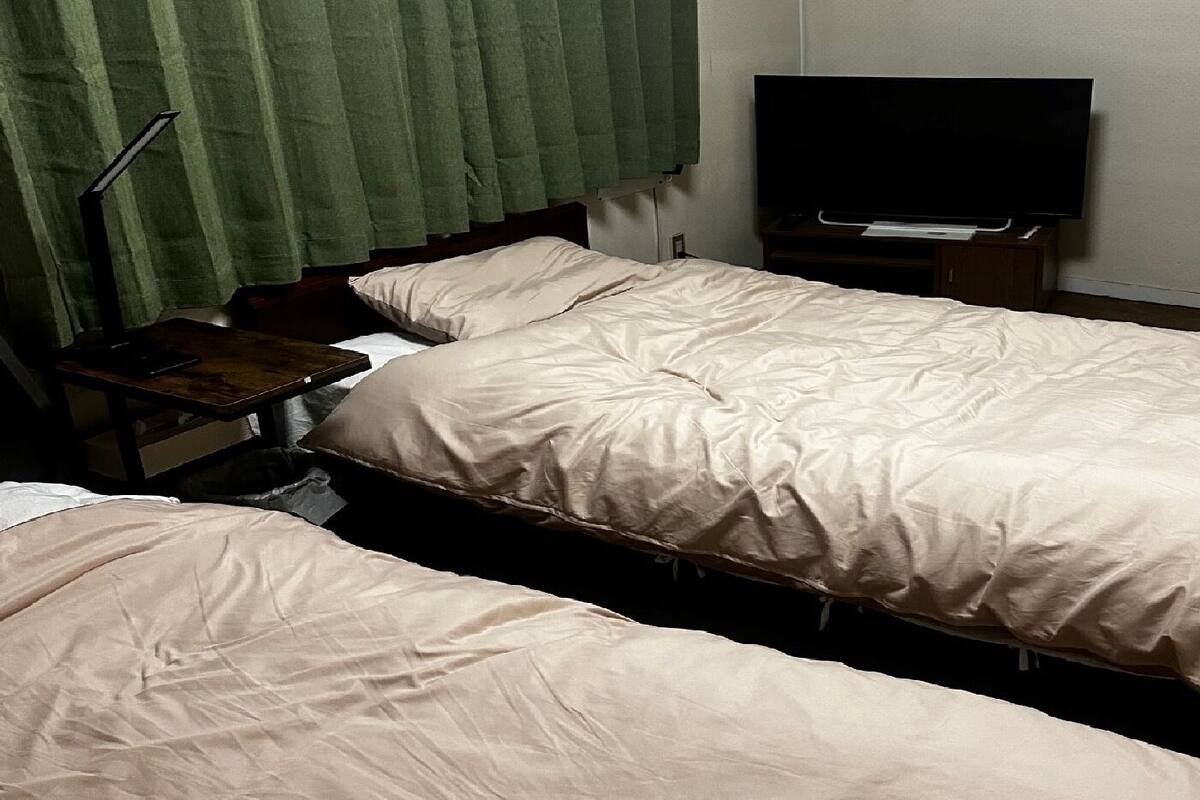 A hotel room with two beds, a desk with a chair, a television, and green curtains.