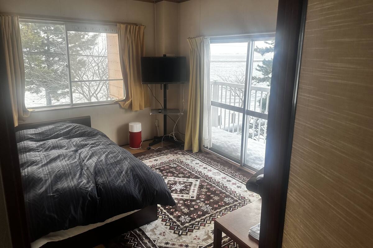 A bedroom with a bed, a TV, a heater, and large windows with curtains.