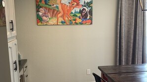 Ein Essbereich mit Holztisch und -stühlen, einem Bild an der Wand und einer Küche mit Schränken und einem Kühlschrank.