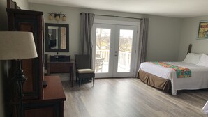 Ein Hotelzimmer mit Bett, Schreibtisch, Stuhl, Lampe, Spiegel und Blick ins Freie durch eine Glastür.