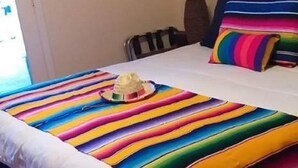 Een slaapkamer met een bed, een gestreept dekbed, een nachtkastje, een stoel en een raam.