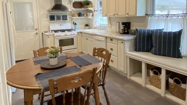 A kitchen with a wooden dining table, chairs, a stove, and white cabinets.