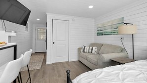 A modern, white-themed room with a bed, a sofa, a TV mounted on the wall, and a small table. - Romantic Island Getaway for 2 on Navarre Beach. (Navarre)