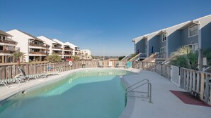 A swimming pool with lounge chairs and a wooden deck, surrounded by multi-story buildings with balconies. - Romantic Island Getaway for 2 on Navarre Beach. (Navarre)