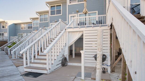 A wooden deck leading to a building with multiple windows and a white railing. - Romantic Island Getaway for 2 on Navarre Beach. (Navarre)