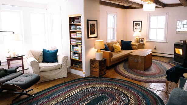 A cozy living room with a sofa, armchair, and a bookshelf. There is a fireplace and a window providing natural light. - Authentic farmhouse for those who love cozy, quirky, historical imperfection (Randolph Center)