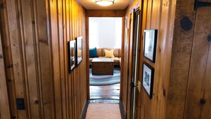 A wooden hallway with framed pictures on the walls, leading to a room with a sofa and a window. - Authentic farmhouse for those who love cozy, quirky, historical imperfection (Randolph Center)