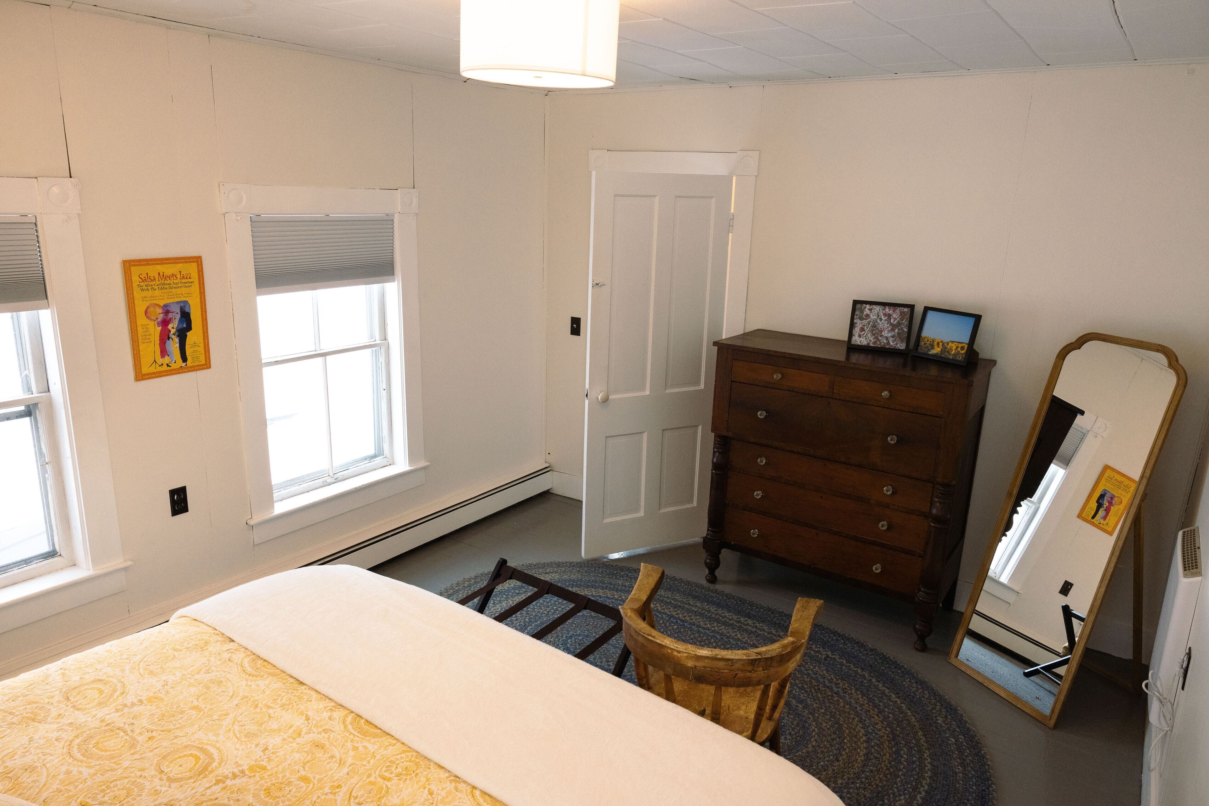 A bedroom with a bed, a dresser, a chair, a mirror, and a window.