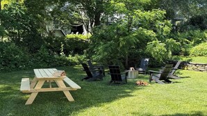 A picnic setup with a wooden table and chairs in a grassy area surrounded by trees. - Authentic farmhouse for those who love cozy, quirky, historical imperfection (Randolph Center)