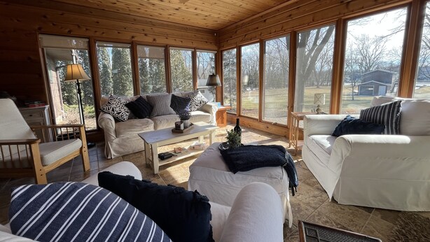 Un interior de cabaña acogedor, con techo de madera, ventanas amplias y mobiliario en tonos blanco y a rayas.