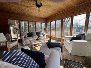 Un interior de cabaña acogedor, con techo de madera, ventanas amplias y mobiliario en tonos blanco y a rayas.