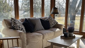 Una sala de estar acogedora con un sofá color beige, cojines estampados, una mesa de centro de madera y una lámpara.