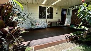 A covered porch with a wooden deck, a dining table with chairs, and potted plants.