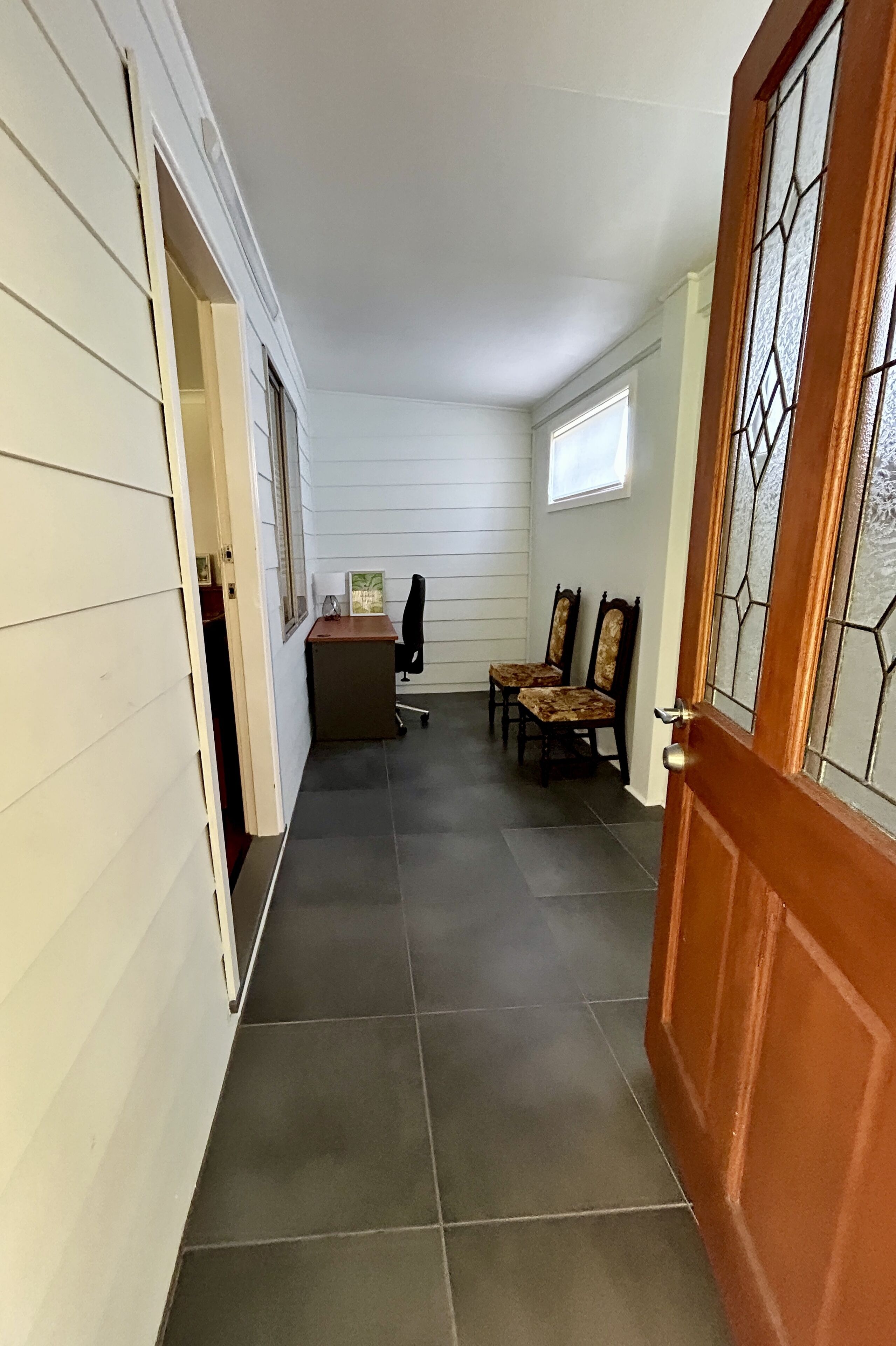 A hallway with a desk, two chairs, and a door with a glass panel.