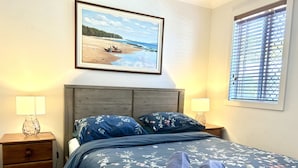 A bedroom with a bed, two nightstands, a lamp, a painting, and a window with blinds.