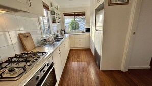 A kitchen with white cabinets, a stainless steel refrigerator, a gas stove, and wooden flooring.