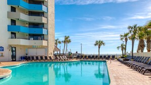 A hotel pool area with a clear view of the ocean, a tall building with blue balconies, and a sign for the "TOWEL HUT". - Luxury Beachfront Studio, Endless Ocean Views, Resort Amenities, Newly Remodeled (Myrtle Beach)