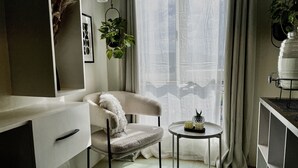 Una habitación moderna con un sofá blanco, una mesita redonda con adornos, un ventanal con cortinas translúcidas y una planta colgante del techo.