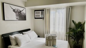 Una cama bien hecha con sábanas blancas, un cuadro de un toro en la pared, una ventana con cortinas y una planta en maceta.