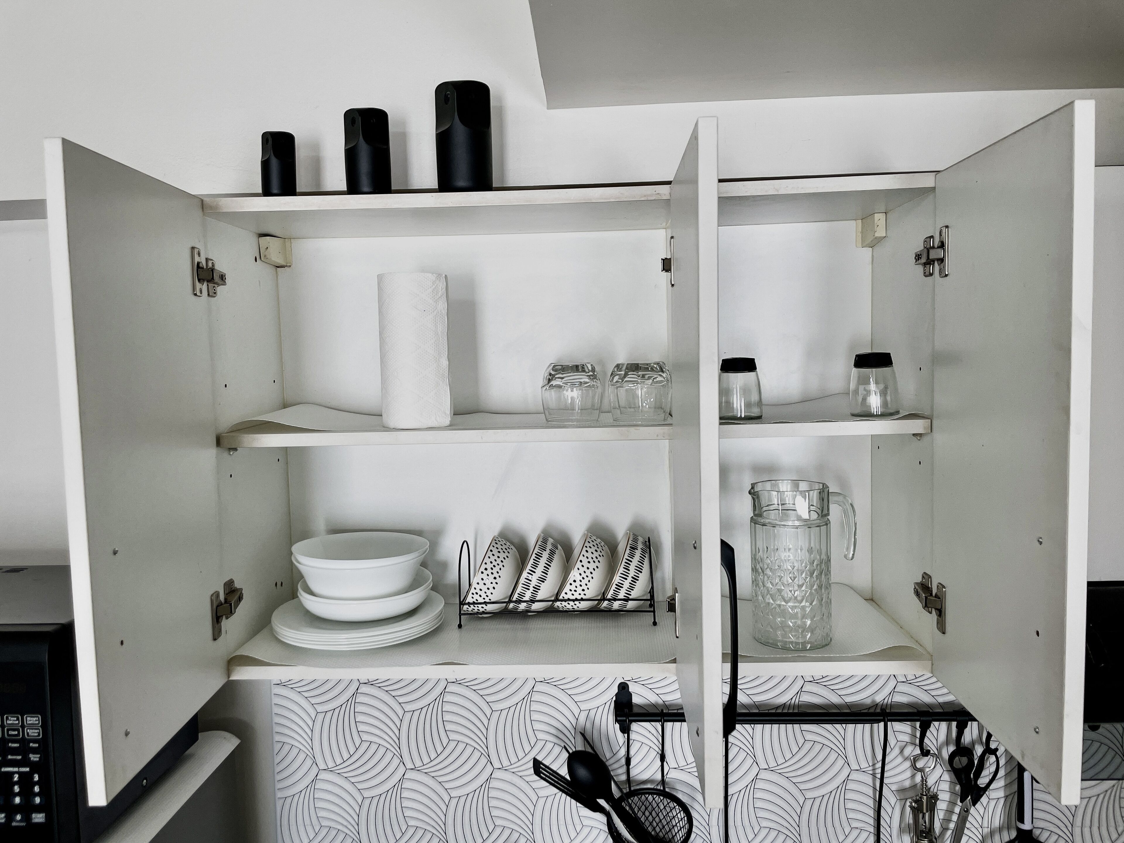 A kitchen with white cabinets, a microwave, a kettle, and various kitchen utensils.