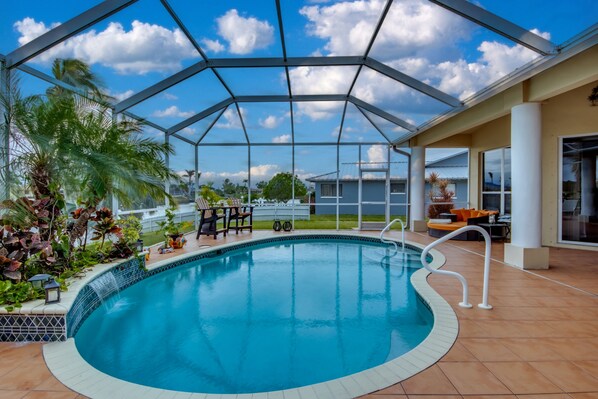 Ein überdachter Pool mit Glasdach, umgeben von Palmen und Gartenmöbeln.