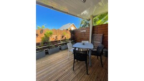 Une terrasse en bois avec une table et des chaises, entourée de plantes en pot et d’une clôture en bois.