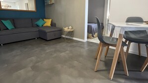 Un salon moderne avec un canapé gris, une petite table ronde et un coin repas comprenant une table et des chaises.