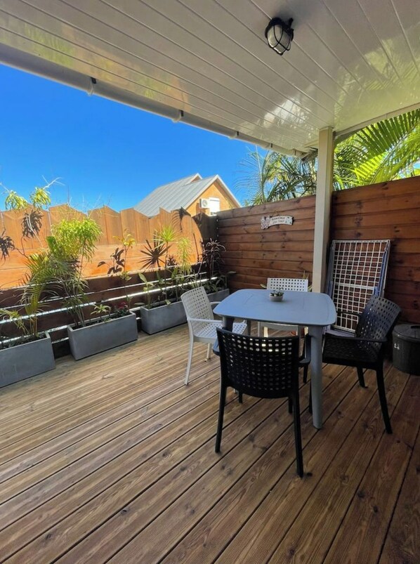 A wooden deck with a table and chairs, surrounded by potted plants and a wooden fence.