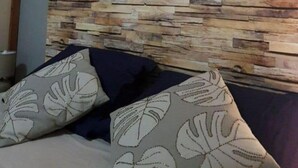 Une chambre avec un mur revêtu de panneaux en bois, un lit agrémenté d’oreillers à motifs et un objet décoratif en fibres tressées accroché au mur.
