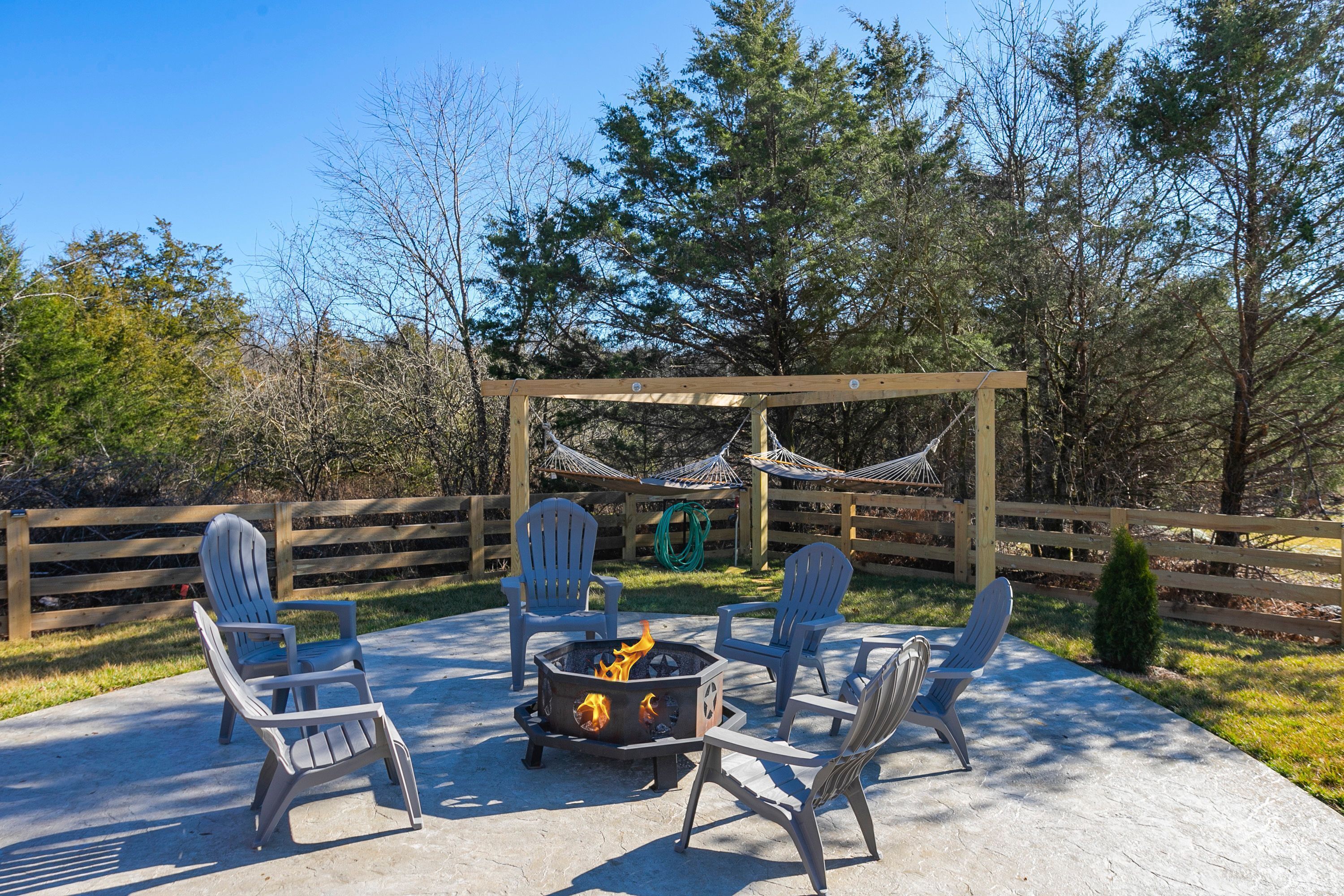 A patio with Adirondack chairs, a fire pit, and a wooden pergola with hammocks.