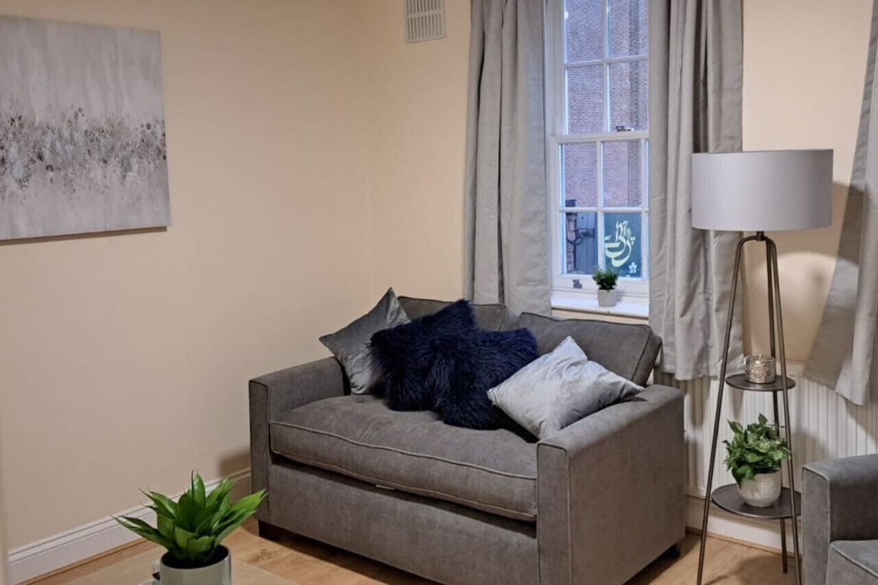 Een woonkamer met een grijze bank, een vloerlamp en een raam met gordijnen.