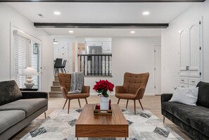 Een moderne woonkamer met een bank, twee fauteuils, een salontafel met een vaas rode bloemen, en een kamerbreed tapijt.