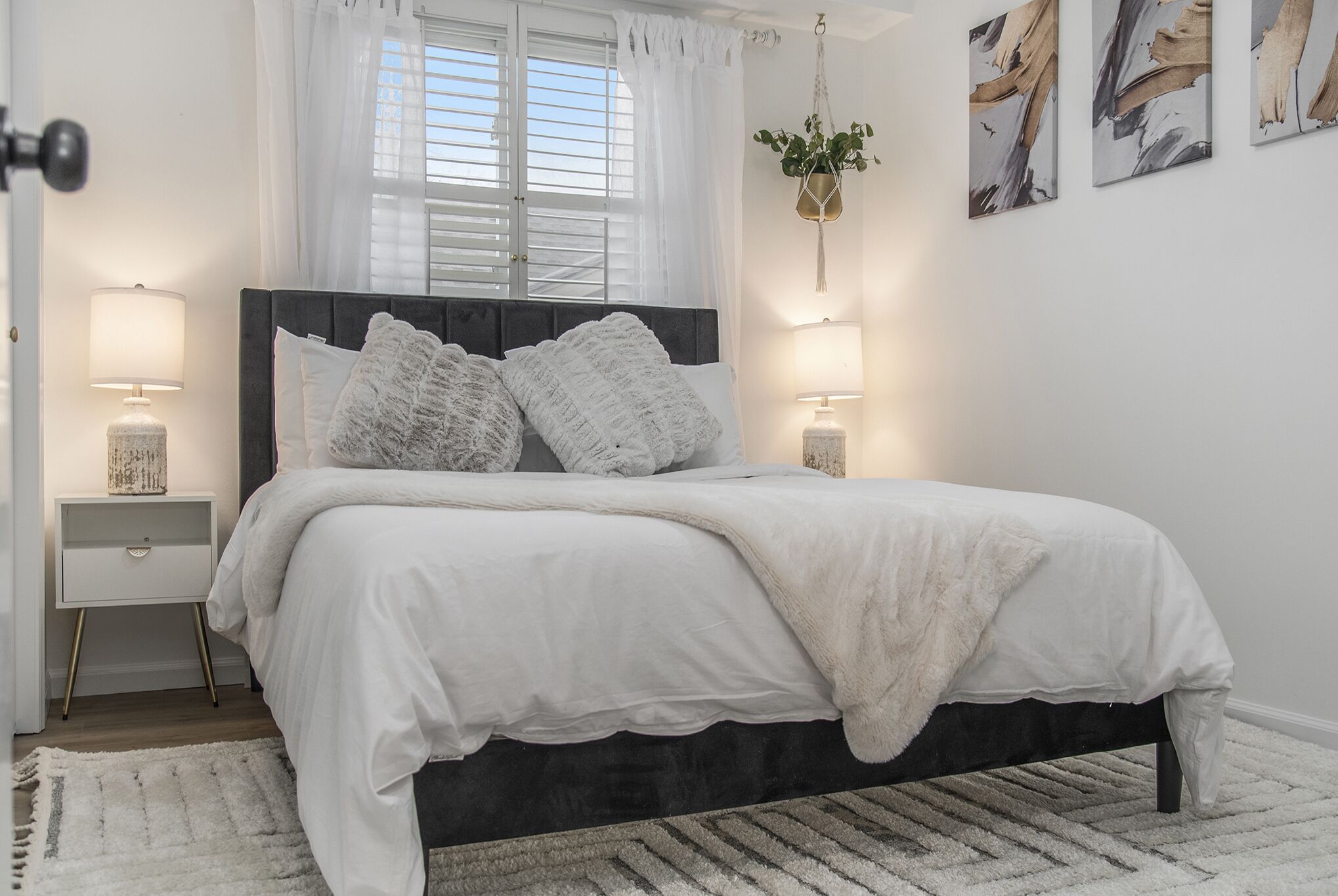 A bedroom with a bed, bedside tables, a window with curtains, and wall art.