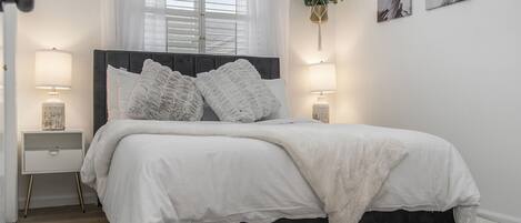 A bedroom with a bed, bedside tables, a window with curtains, and wall art.