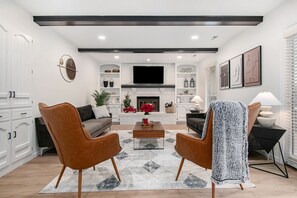 Een moderne woonkamer met een open haard, twee fauteuils, een salontafel en een televisie die boven de haard is bevestigd.