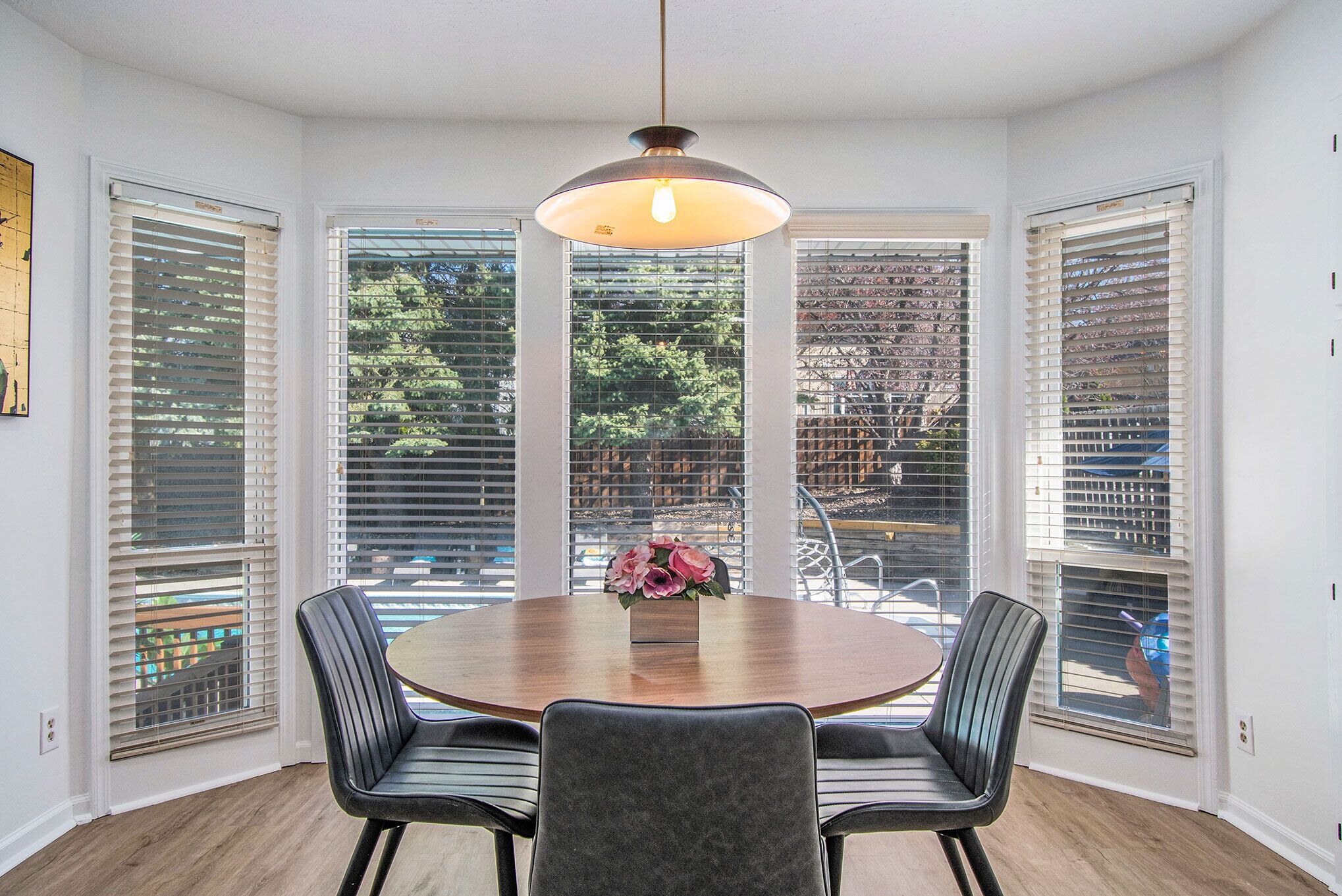 A dining area with a round table, four chairs, and a hanging light fixture.