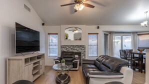 A modern living room with a flat-screen TV, leather sofas, a glass coffee table, and a ceiling fan. - Luxury 4/bed w/Pool & Putt Grn (Peoria)