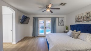 A bedroom with a large bed, a ceiling fan, a TV mounted on the wall, and a view of a swimming pool through a glass door. - Luxury 4/bed w/Pool & Putt Grn (Peoria)
