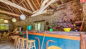 A rustic bar area with wooden stools, a stone wall, and a variety of bottles and glasses on shelves. - Luxurious apartment in Saint-Affrique (Saint-Affrique)