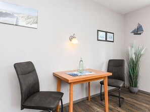 A room with a wooden table, two chairs, a wall-mounted light, framed pictures, and a potted plant.