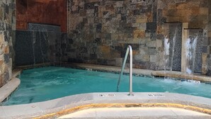 Piscina interior con paredes de piedra, una escalera de metal, agua cristalina y un letrero que dice 'NO DIVING'.