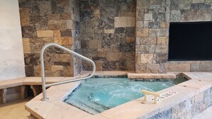 Un área de spa con pared de piedra, jacuzzi y una escalera que conduce a un balcón.