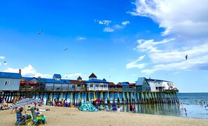 Eine Pier mit Strandunterkünften, darunter ein sichtbarer Geldautomat, und ein Sandstrand mit Menschen und Sonnenschirmen.