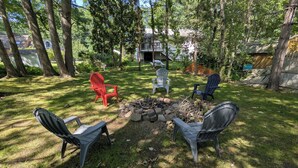 A backyard with a fire pit surrounded by four Adirondack chairs, a red chair, and a blue chair. - Spacious & sunny, 7 minutes from the beach! (Old Orchard Beach)