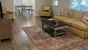 Un salón espacioso con suelo de madera, un sofá color beige, una mesita de centro y una alfombra estampada.