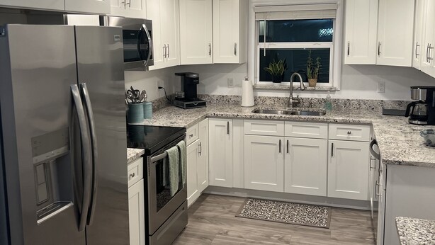 Una cocina moderna con armarios blancos, electrodomésticos de acero inoxidable, horno empotrado y una ventana sobre el fregadero.
